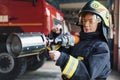 Hose in hands. Female firefighter in protective uniform standing near truck