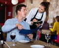 Hospitable waitress helping handsome man with menu, taking order in restaurant Royalty Free Stock Photo