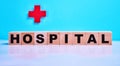 Hospital inscription on wooden cubes on a blue background, on the background of a red cross. Medical concept