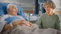 Hospital Ward: Elderly Man Resting in Bed, His Caring Beautiful Wife Supports Him Sitting Beside, Royalty Free Stock Photo