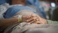 Hospital Ward: Focus on Hands of Elderly Man Resting in Bed, His Caring Wife Supports Him By Sitti Royalty Free Stock Photo