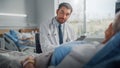 Hospital Ward: Friendly Doctor Talks to Beautiful Senior Female Patient Resting in Bed, Explains Royalty Free Stock Photo