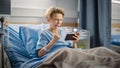 Hospital Ward: Handsome Young Boy Resting in Bed, Uses Smartphone, Wins in Online Video Game on In Royalty Free Stock Photo