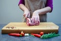 The hostess in the kitchen cuts pork with a knife, prepares food. On a cutting board, spices, chili peppers, rosemary, cherry Royalty Free Stock Photo