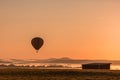 Hot air balloon is basked in a golden glow as it slowly ascends over a fog-filled valley on an early fall mo