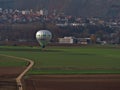 Hot air balloon branded by public utility company Stadtwerke Stuttgart about to land on field near town Besigheim with walkers .
