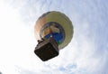 Hot-air balloon drifting in the sky, people looking out from a basket, view from below