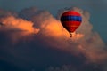 Fantastical image of an ornate red and blue hot air balloon floating high in beautiful storm clouds glowing at sunset
