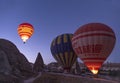 a hot air balloon full of tourists, about to take off at dawn between fairy chimneys, service vans around the balloons and other