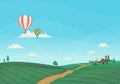 Hot air balloons flying over agricultural fields, roads and a small village or farm. Blue sky with clouds in the background.