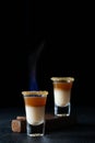 Hot alcoholic shot with baileys and whiskey with fire on a black background, close-up