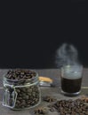 Hot amarican black coffee glass with smoke and coffee beans in jar on rustic wooden table.Closeup view with black copy space Royalty Free Stock Photo