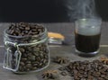 Hot american black coffee with smoke and coffee beans in glass jar on wooden table.Closeup view with dark copy space Royalty Free Stock Photo