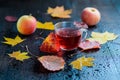 Hot autumn vitamin herbal tea in transparent cup with water vapor with autumn leaves and apples