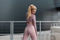 Hot beautiful blonde fitness model woman with sexy slim body in stylish sportswear stands in the city near modern building and Royalty Free Stock Photo