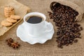 Hot black coffee in white elegant cup with saucer, sweet cookies and scattering of coffee beans on rural sackcloth background. Royalty Free Stock Photo