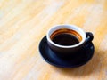 Hot black intense Americano coffee in a black coffee cup with handle placed on a wooden table