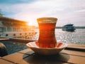 Hot black Turkish tea in traditional glass on table in front of blurry Istanbul cityscape and sailing ferry boats in bosphorus in