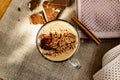 Hot cappuccino with chocolate chips on top of the foam, a cinnamon stick, Golden sugar beads and a sweet waffle next to it