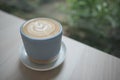 Hot cappuccino coffee cup with tree shape latte art milk foam on wood table near window in garden at cafe restaurant Royalty Free Stock Photo