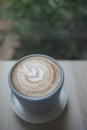 Hot cappuccino coffee cup with tree shape latte art milk foam on wood table near window in garden at cafe restaurant