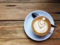 Hot cappuccino coffee in white cup and saucer with spoon on wooden table background. Art of milk foam drawing like white heart on Royalty Free Stock Photo