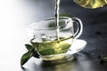 Hot chinese green tea with mint, with splash pouring from the kettle into the cup, steam rises, dark background, selective focus