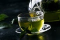 Hot chinese green tea with mint, with splash pouring from the kettle into the cup, steam rises, dark background, selective focus Royalty Free Stock Photo