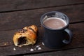 Hot chocolate in a blue-grey ceramic mug next to a half of chocolate croissant isolated on rustic dark brown wood table Royalty Free Stock Photo