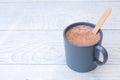 Hot chocolate in a blue-grey ceramic mug with wooden stirrer on white painted wood. Space for text