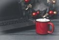 Hot chocolate or coffee and marshmallows next to a spruce Christmas wreath with red balls and a laptop on a gray background Royalty Free Stock Photo