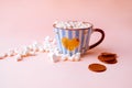 Hot chocolate drink with marshmallows and chocolate crisps in blue striped mug on pastel pink background