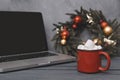 Hot chocolate and marshmallows next to a gray laptop, spruce Christmas wreath with gold red balls on a gray background,  copy Royalty Free Stock Photo