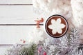 Hot chocolate with snowflake marshmallow, top view with snowy branches and blanket against white wood