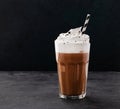 Hot chocolate with whipped cream in a tall glass on a dark background. Front view and copy space