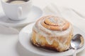 Hot cinnamon bun with sugar creamy icing on white plate. Sweet breakfast or snack with a cup of coffee. Royalty Free Stock Photo