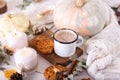 Hot cocoa with cookies in a white mug surrounded by autumn leaves and pumpkins