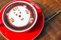 Hot cocoa and face cat milk foam in the red cup on wood background Royalty Free Stock Photo