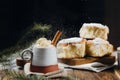 A hot cocoa with whipped cream, cinnamon stick and fresh Christmas buns with powder and over festive table, sugar powder is