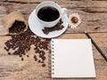 Hot coffee cup with coffee bean and notebook on wooden table. Royalty Free Stock Photo