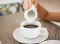 Hot coffee with one hand pouring milk on breakfast table