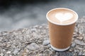 Hot coffee paper cup against river background, heart shape latte coffee art. Love, holiday, Valentine day and free plastic