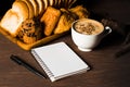 Hot coffee in white cup, with bakery and coffee beans in hemp bag, with notebook placed on dark brown wood table,Beauty concept of Royalty Free Stock Photo