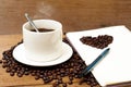 Hot Coffee in white cup and coffee beans heart shape on the note book with pen Royalty Free Stock Photo