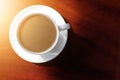 Hot coffee in a white cup placed on a brown wooden table, one side has a warm light and the other side is dark. Royalty Free Stock Photo