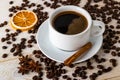 Hot coffee in white elegant cup with saucer on a background of coffe beans over a white wooden table. Coffee with cinnamon, anise Royalty Free Stock Photo