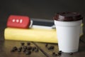 Hot coffee white plastic cup with brown cap and car key and mobile and blank yellow book cover on old wooden table with low light. Royalty Free Stock Photo
