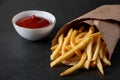 Hot crispy fries in a paper bag on black background. Tasty american fast food.