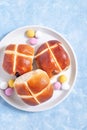 Hot cross buns on white plate with chocolate candy eggs. Traditional easter food, vertical, top view Royalty Free Stock Photo