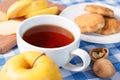 Hot cup of black tea on the table with apples and cookies on blue patchwork tablecloth